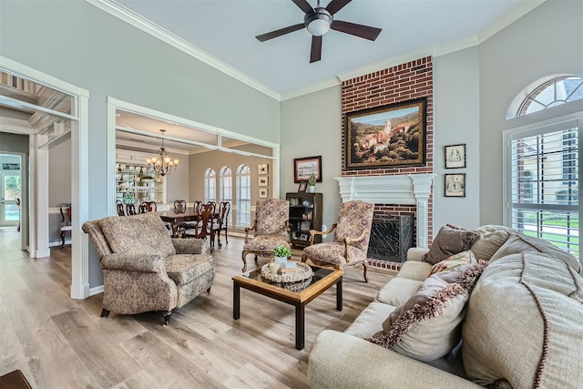 living room with crown molding, ceiling fan with notable chandelier, light wood-type flooring, and a brick fireplace