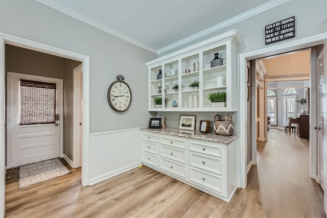 bar with ornamental molding, white cabinetry, light stone counters, and light wood-type flooring