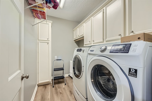 clothes washing area featuring a textured ceiling, washing machine and dryer, light hardwood / wood-style floors, and cabinets