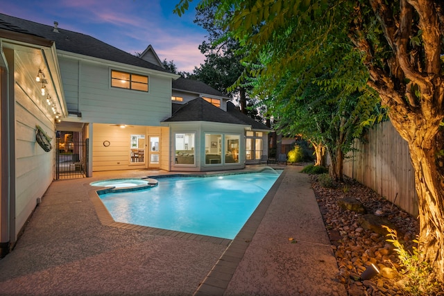 pool at dusk featuring an in ground hot tub and a patio