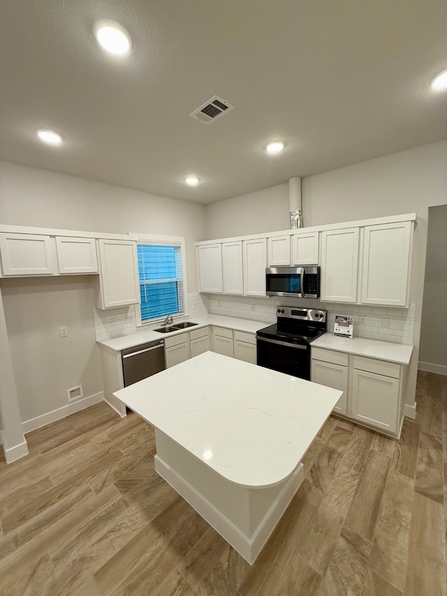 kitchen featuring white cabinetry, sink, decorative backsplash, appliances with stainless steel finishes, and light wood-type flooring