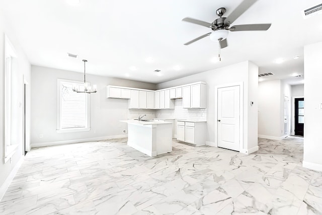 kitchen with tasteful backsplash, a kitchen island with sink, white cabinetry, decorative light fixtures, and ceiling fan with notable chandelier