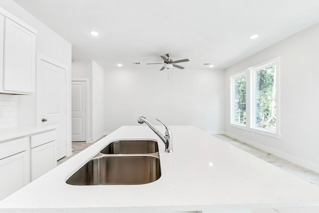 kitchen featuring light stone counters, sink, an island with sink, white cabinets, and ceiling fan