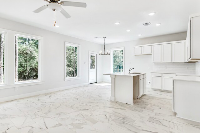 kitchen featuring sink, tasteful backsplash, decorative light fixtures, an island with sink, and white cabinets