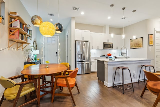 kitchen featuring white cabinetry, pendant lighting, appliances with stainless steel finishes, and a kitchen island with sink