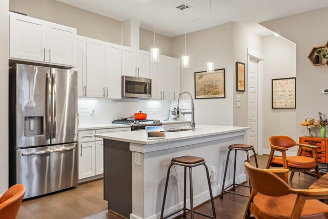 kitchen featuring sink, stainless steel appliances, decorative light fixtures, and an island with sink