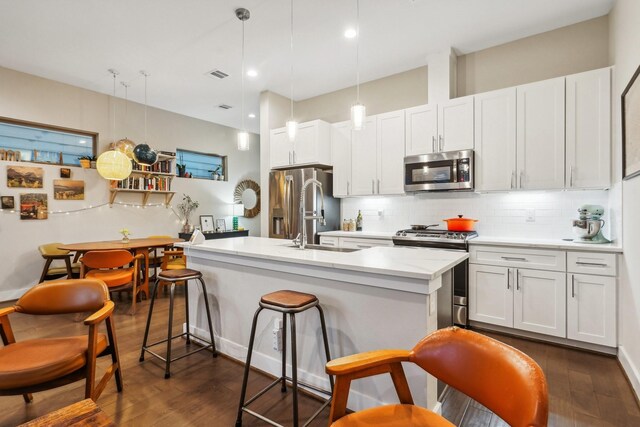 kitchen featuring a kitchen island with sink, white cabinets, pendant lighting, and appliances with stainless steel finishes