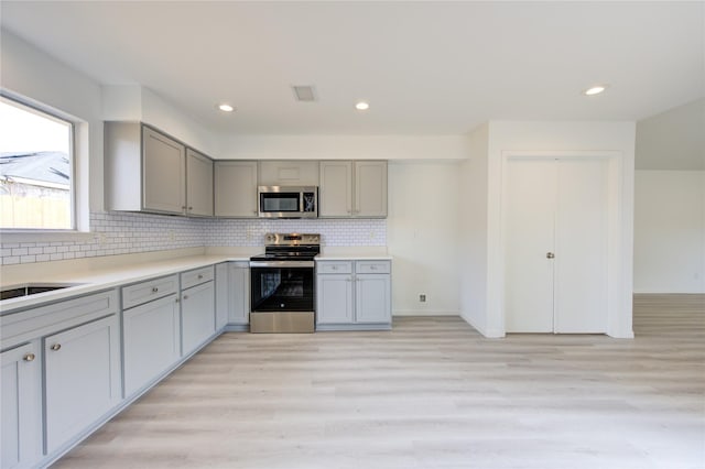 kitchen with stainless steel appliances, tasteful backsplash, gray cabinetry, and light hardwood / wood-style flooring