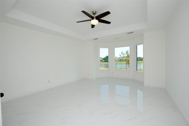 spare room featuring a water view, a tray ceiling, and ceiling fan