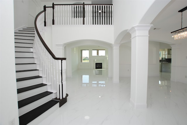 foyer entrance featuring ornate columns, a towering ceiling, and a chandelier