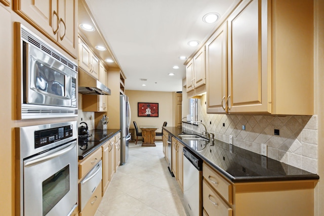 kitchen with tasteful backsplash, appliances with stainless steel finishes, light brown cabinetry, dark stone counters, and sink