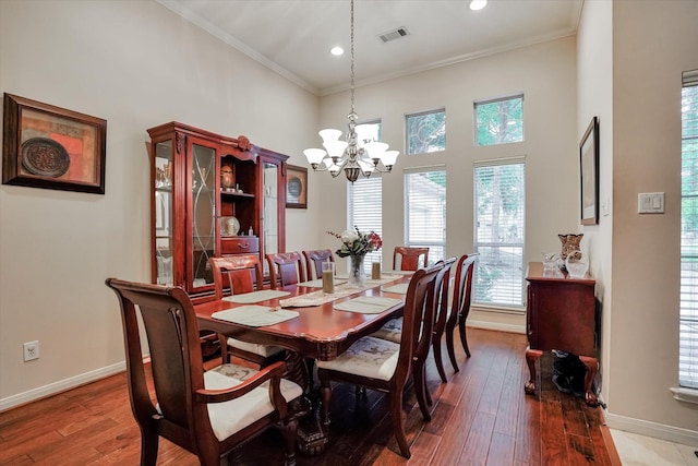 dining area with a notable chandelier, crown molding, hardwood / wood-style flooring, and a towering ceiling