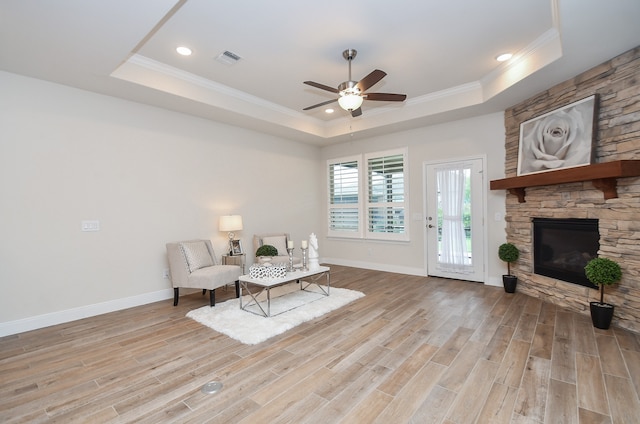 sitting room with light hardwood / wood-style flooring, a stone fireplace, a tray ceiling, and ceiling fan