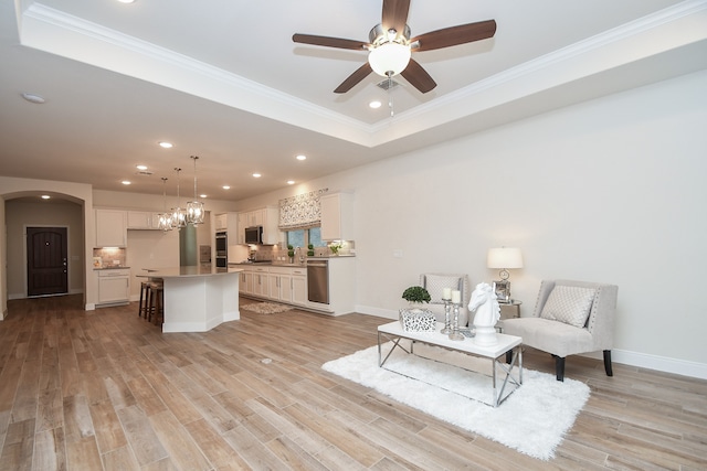 living room with crown molding, ceiling fan with notable chandelier, a tray ceiling, and light hardwood / wood-style floors