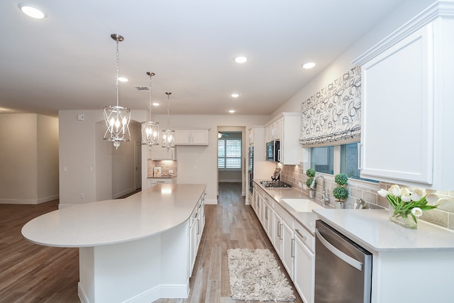 kitchen with appliances with stainless steel finishes, white cabinets, decorative light fixtures, and a kitchen island