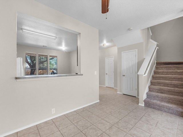 empty room with ceiling fan, a textured ceiling, and light tile patterned floors