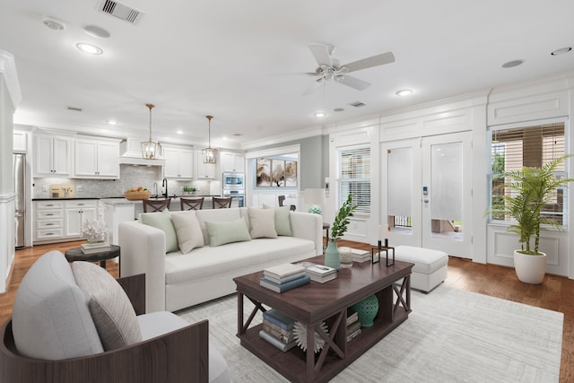 living room featuring ornamental molding, sink, light hardwood / wood-style flooring, and ceiling fan