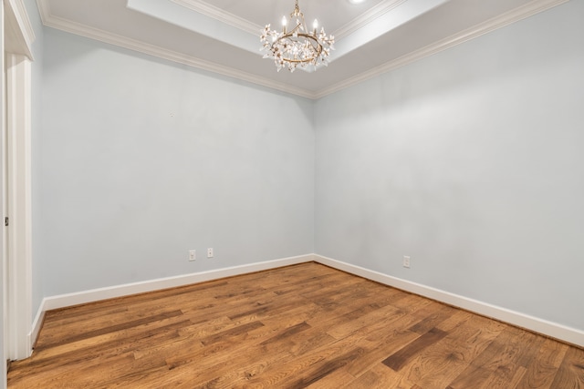 empty room featuring crown molding, a tray ceiling, a chandelier, and wood-type flooring