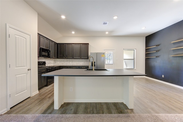 kitchen featuring an island with sink, a breakfast bar, hardwood / wood-style flooring, black appliances, and sink