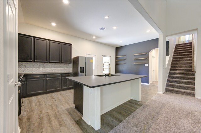 kitchen with a kitchen breakfast bar, light hardwood / wood-style flooring, a center island with sink, sink, and stainless steel fridge with ice dispenser