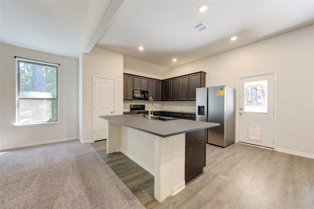 kitchen with black appliances, light wood-type flooring, an island with sink, dark brown cabinetry, and decorative backsplash