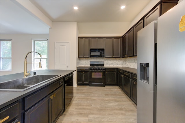 kitchen featuring dark brown cabinets, backsplash, black appliances, light hardwood / wood-style floors, and sink