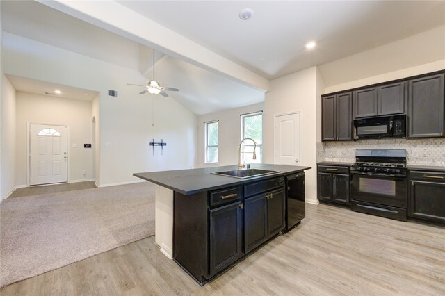 kitchen with black appliances, sink, lofted ceiling with beams, decorative backsplash, and a center island with sink