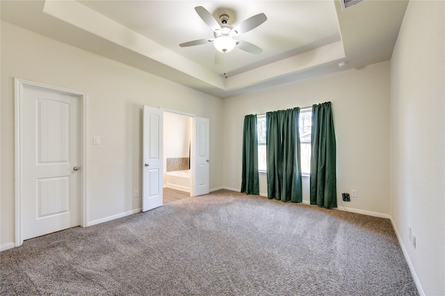 unfurnished bedroom with a raised ceiling, ensuite bathroom, carpet, and ceiling fan