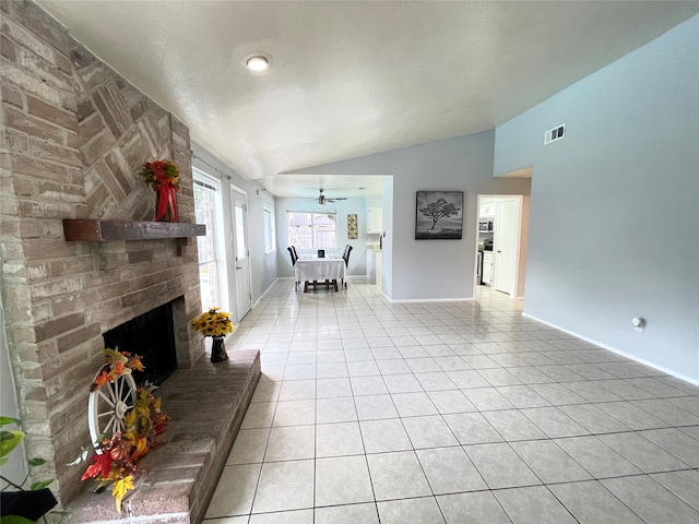 unfurnished living room featuring vaulted ceiling, a brick fireplace, light tile patterned floors, a textured ceiling, and ceiling fan