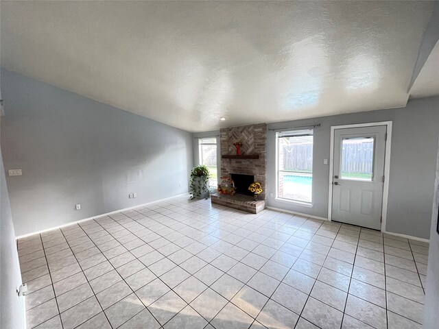 unfurnished living room featuring a stone fireplace, a textured ceiling, and light tile patterned floors