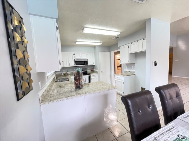 kitchen featuring light stone countertops, appliances with stainless steel finishes, kitchen peninsula, and white cabinetry