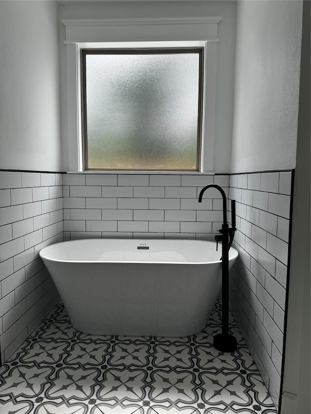 bathroom featuring a freestanding bath, tile patterned flooring, and tile walls