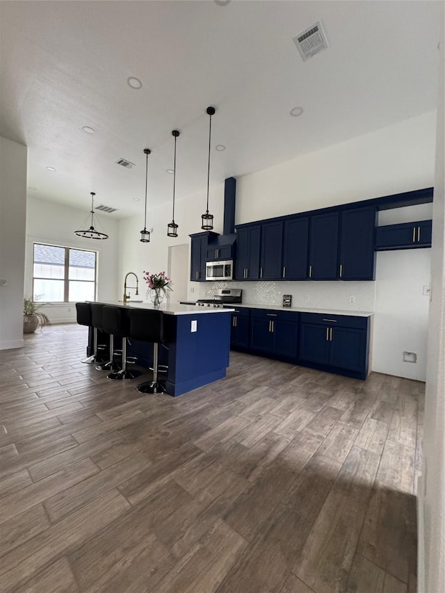 kitchen with a center island with sink, a breakfast bar area, light countertops, visible vents, and appliances with stainless steel finishes