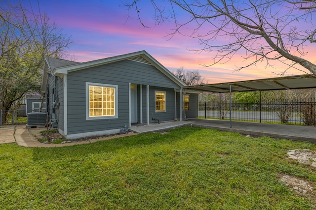 back house at dusk with central air condition unit and a lawn