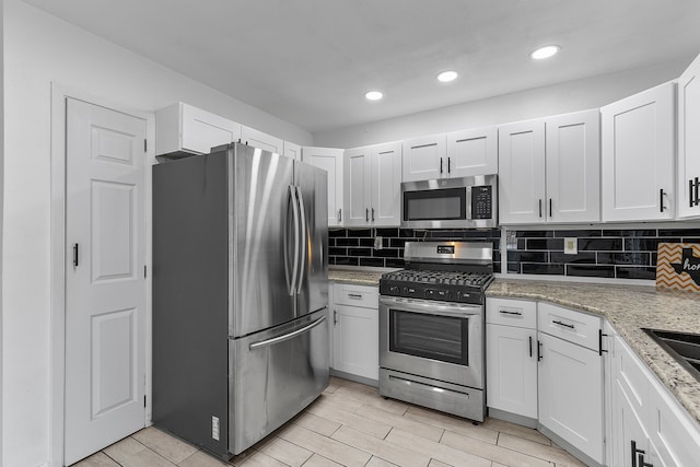 kitchen with appliances with stainless steel finishes, decorative backsplash, white cabinets, and light stone countertops