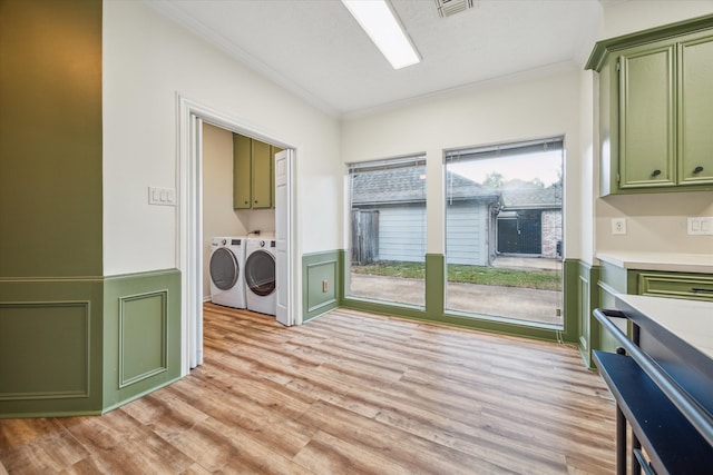 clothes washing area featuring ornamental molding, washer and clothes dryer, light hardwood / wood-style floors, and cabinets