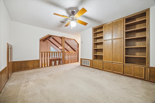 unfurnished living room with light carpet, a textured ceiling, wooden walls, and ceiling fan