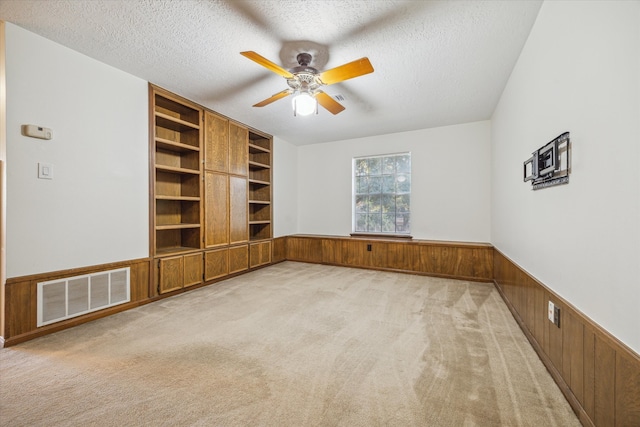 interior space featuring built in shelves, wooden walls, a textured ceiling, and carpet floors