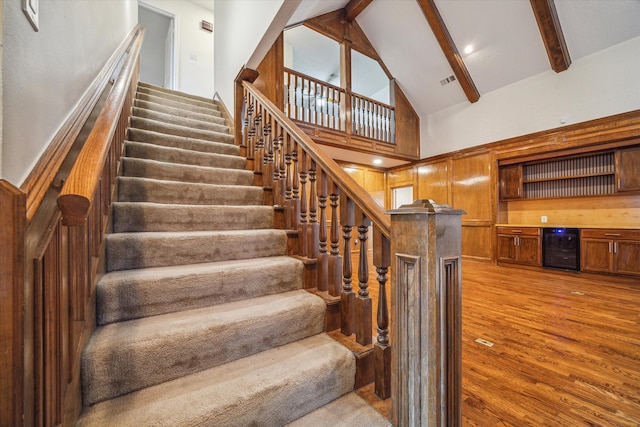 stairway featuring beam ceiling, hardwood / wood-style flooring, high vaulted ceiling, and beverage cooler