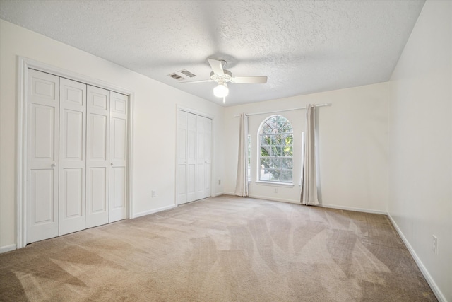 unfurnished bedroom with a textured ceiling, light carpet, two closets, and ceiling fan