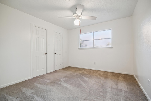 unfurnished bedroom with multiple closets, light carpet, a textured ceiling, and ceiling fan