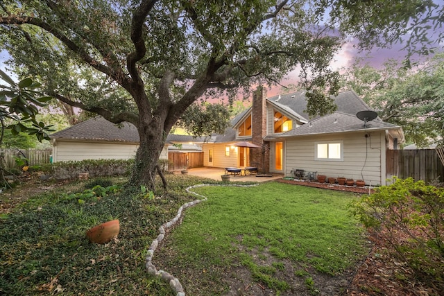 back house at dusk featuring a hot tub, a yard, and a patio area