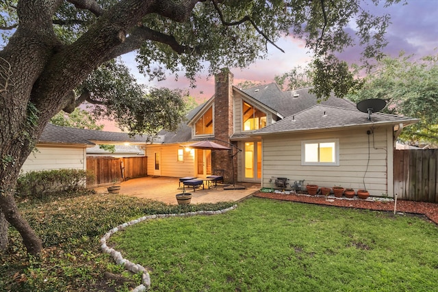 back house at dusk with a patio area and a lawn