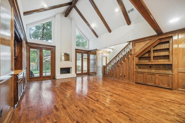 unfurnished living room featuring french doors, hardwood / wood-style flooring, beamed ceiling, a brick fireplace, and high vaulted ceiling