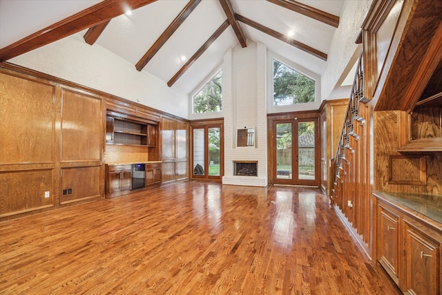 unfurnished living room featuring french doors, beam ceiling, dark wood-type flooring, a brick fireplace, and high vaulted ceiling