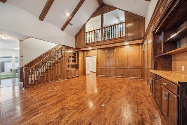 unfurnished living room with hardwood / wood-style floors, beam ceiling, a textured ceiling, high vaulted ceiling, and wooden walls