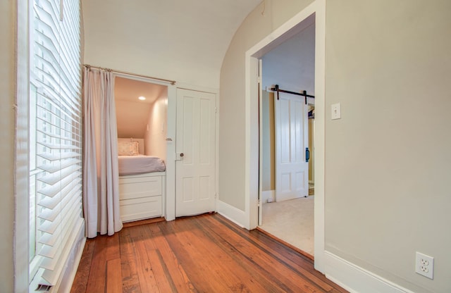 hall with a barn door, wood-type flooring, and vaulted ceiling