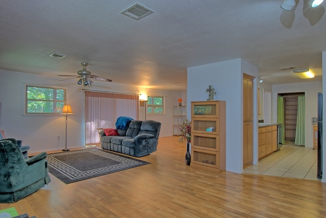 living room featuring a textured ceiling, light wood-type flooring, and ceiling fan