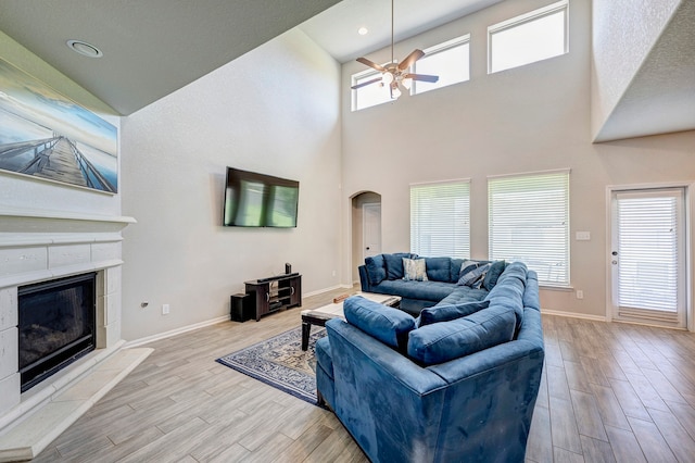 living room with a towering ceiling, a tile fireplace, plenty of natural light, and light wood-type flooring