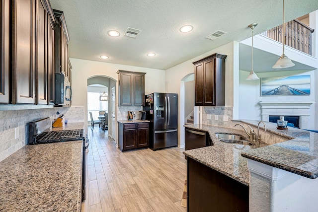 kitchen with hanging light fixtures, stainless steel appliances, dark stone counters, sink, and a textured ceiling